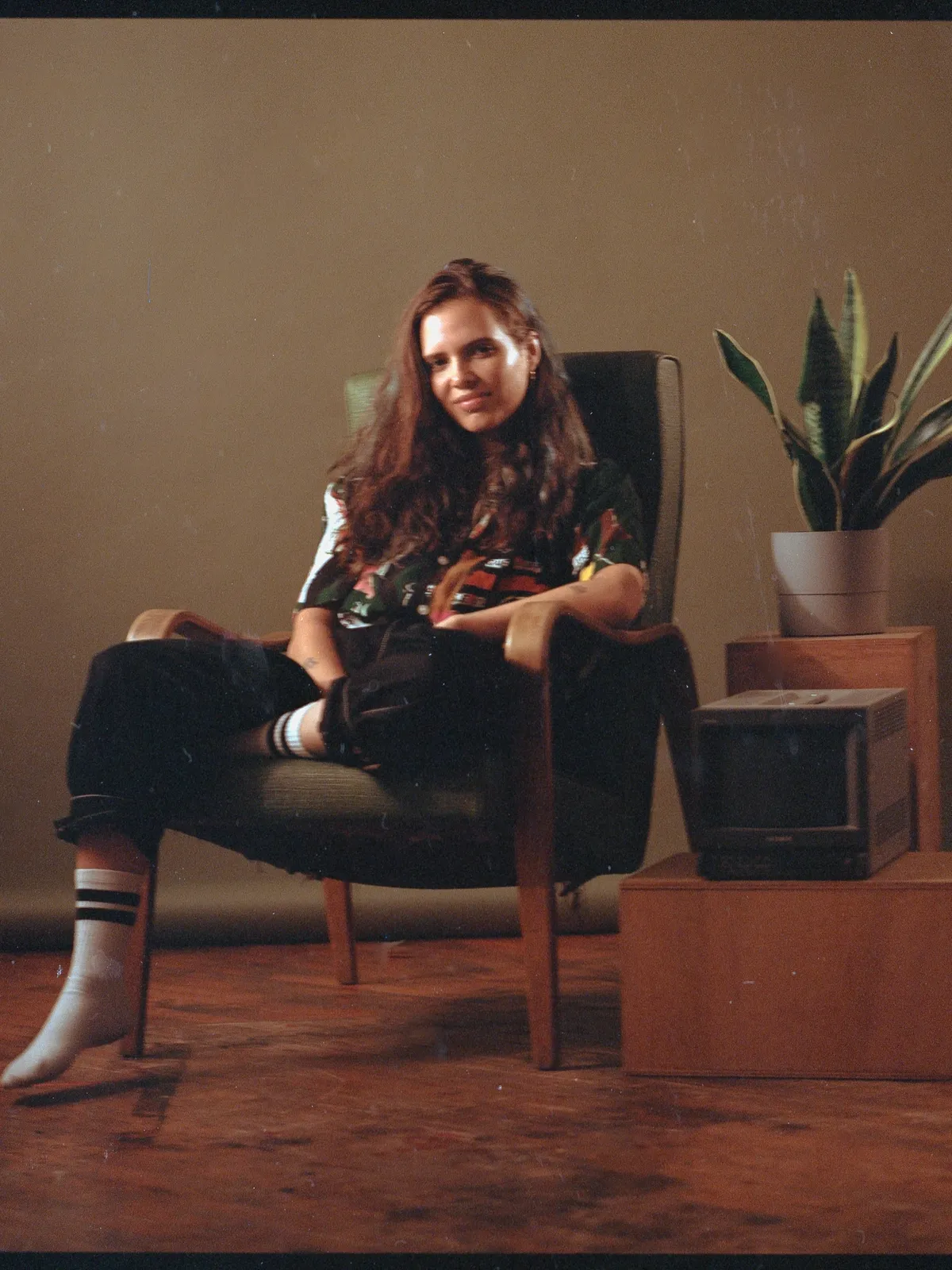 Dionne sitting in an armchair next to a retro TV and a plant
