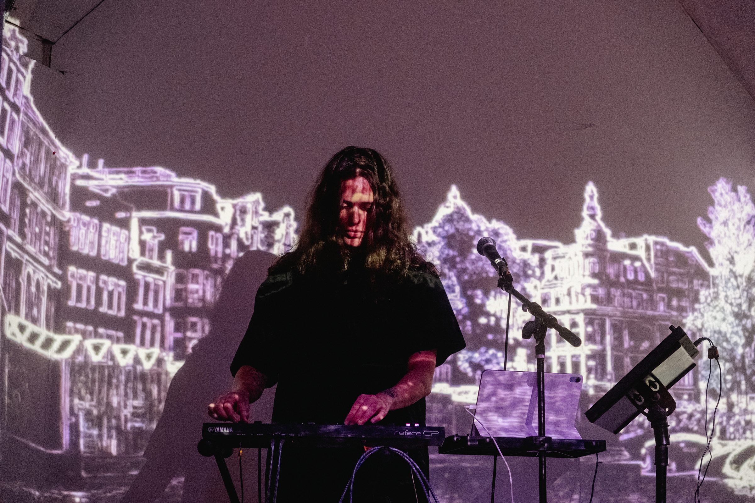 Dionne performing live on synths in front of a projection of Amsterdam canal houses